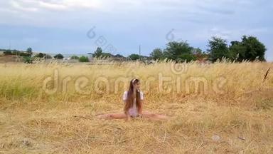 穿着短裤和t恤长发的可爱苗条女孩在田野上用金色的草地做着缠绕和微笑